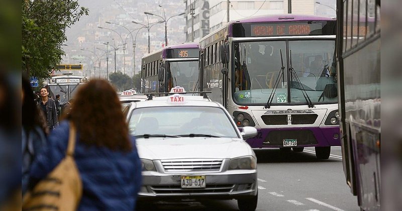 Bus del corredor complementario Morado circulando junto a un taxi en una avenida de Lima